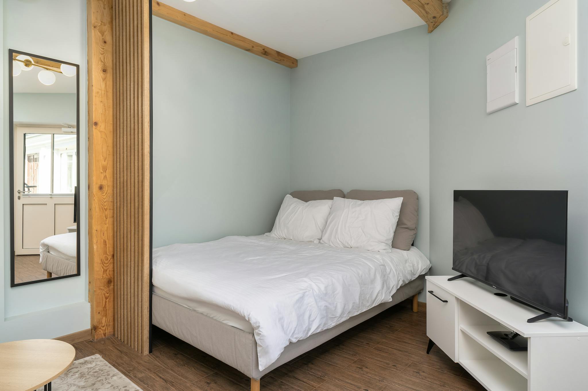 Modern minimalist bedroom with a cozy bed, wood accents, and a flat-screen TV.