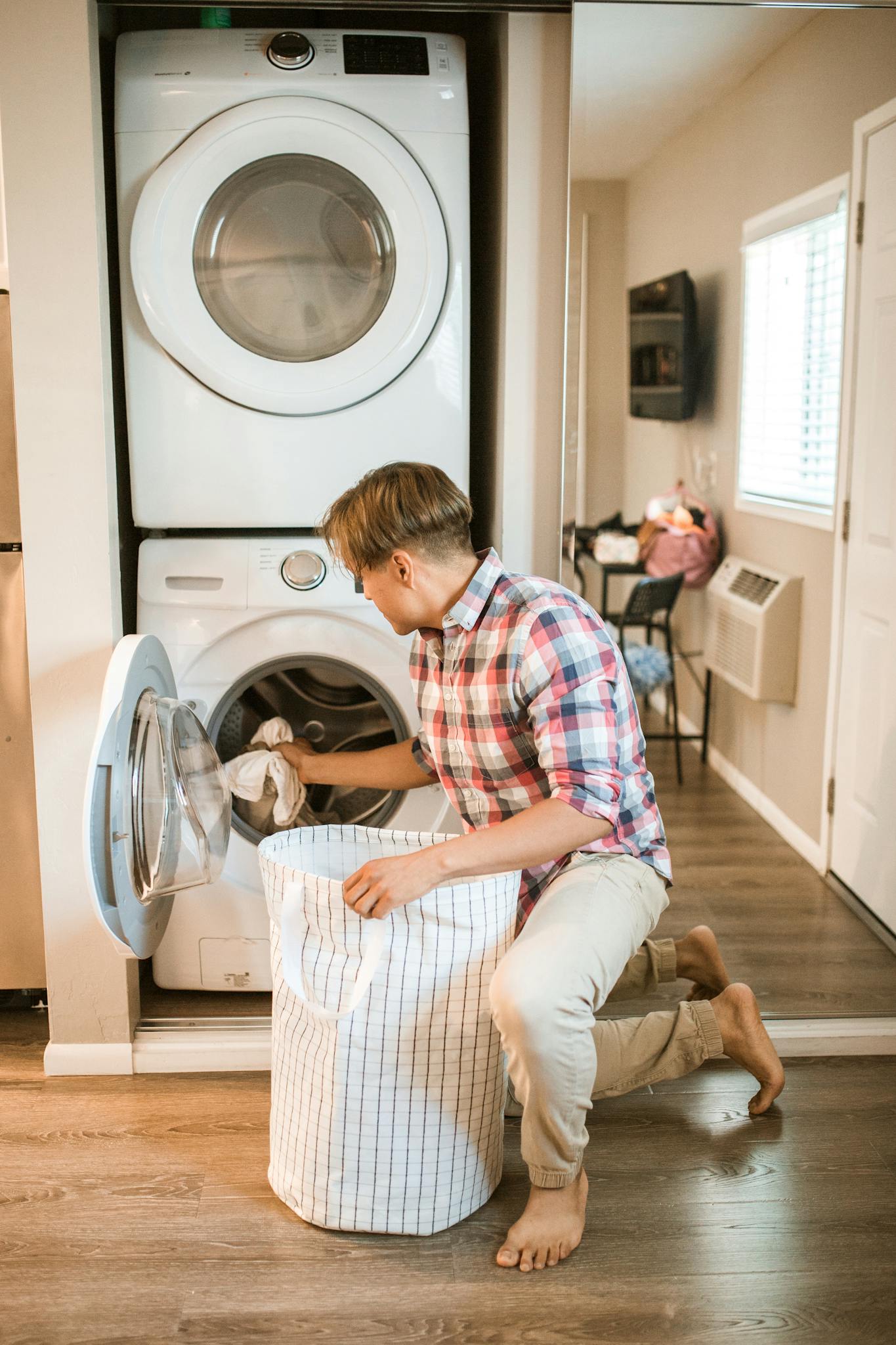 Young man kneeling by washing machine, organizing laundry in cozy home interior.