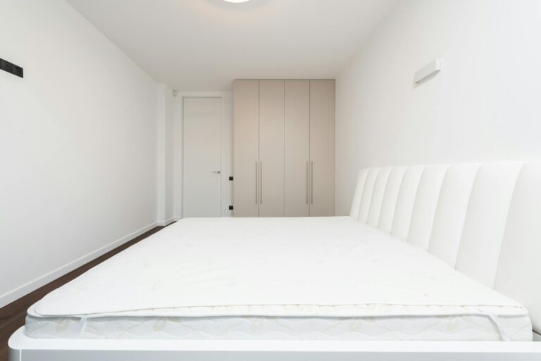 Contemporary minimalist bedroom featuring a white mattress and sleek wardrobe under soft lighting.